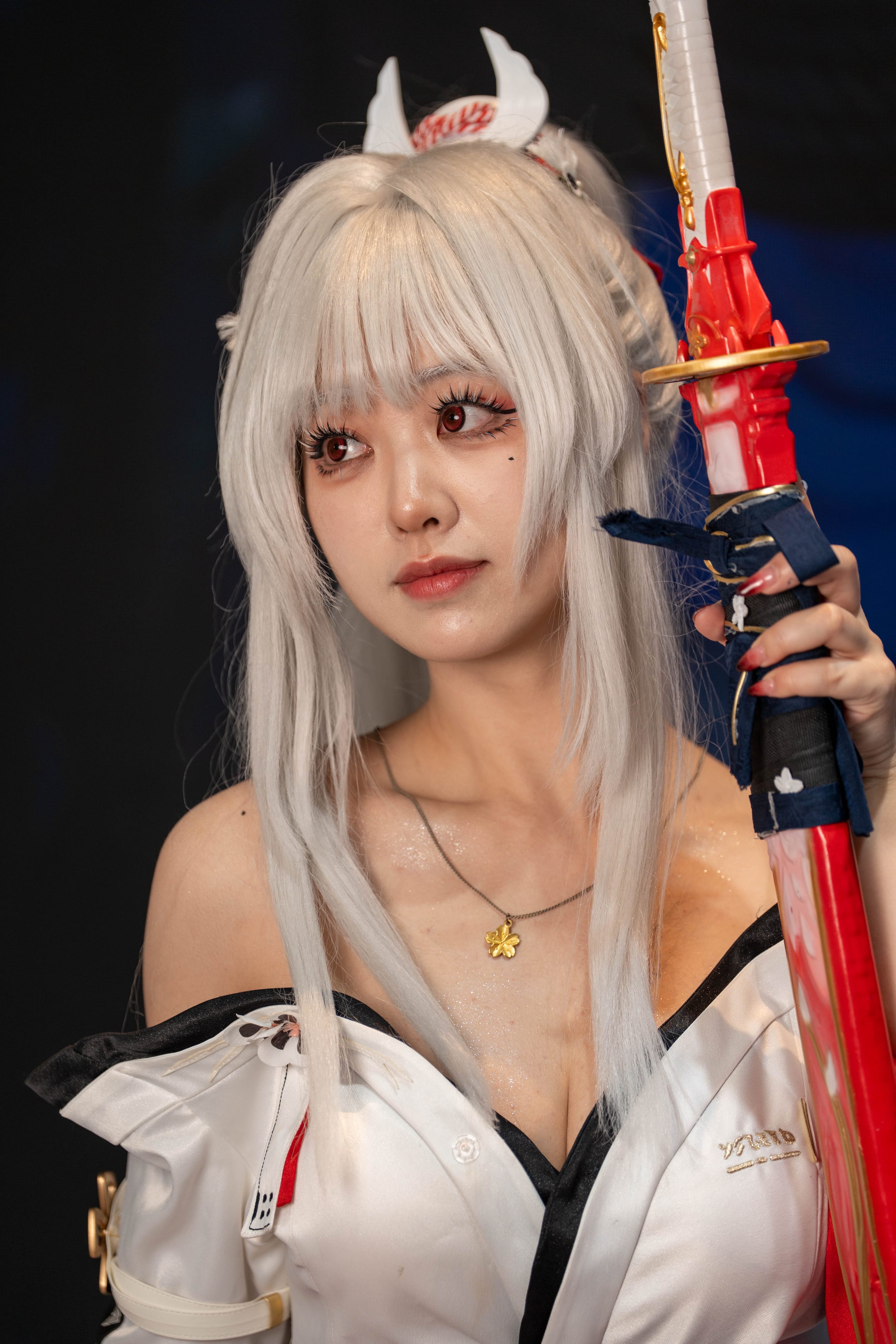 Close portrait of a cosplayer with white hair and small horns holding a red-wrapped sword hilt