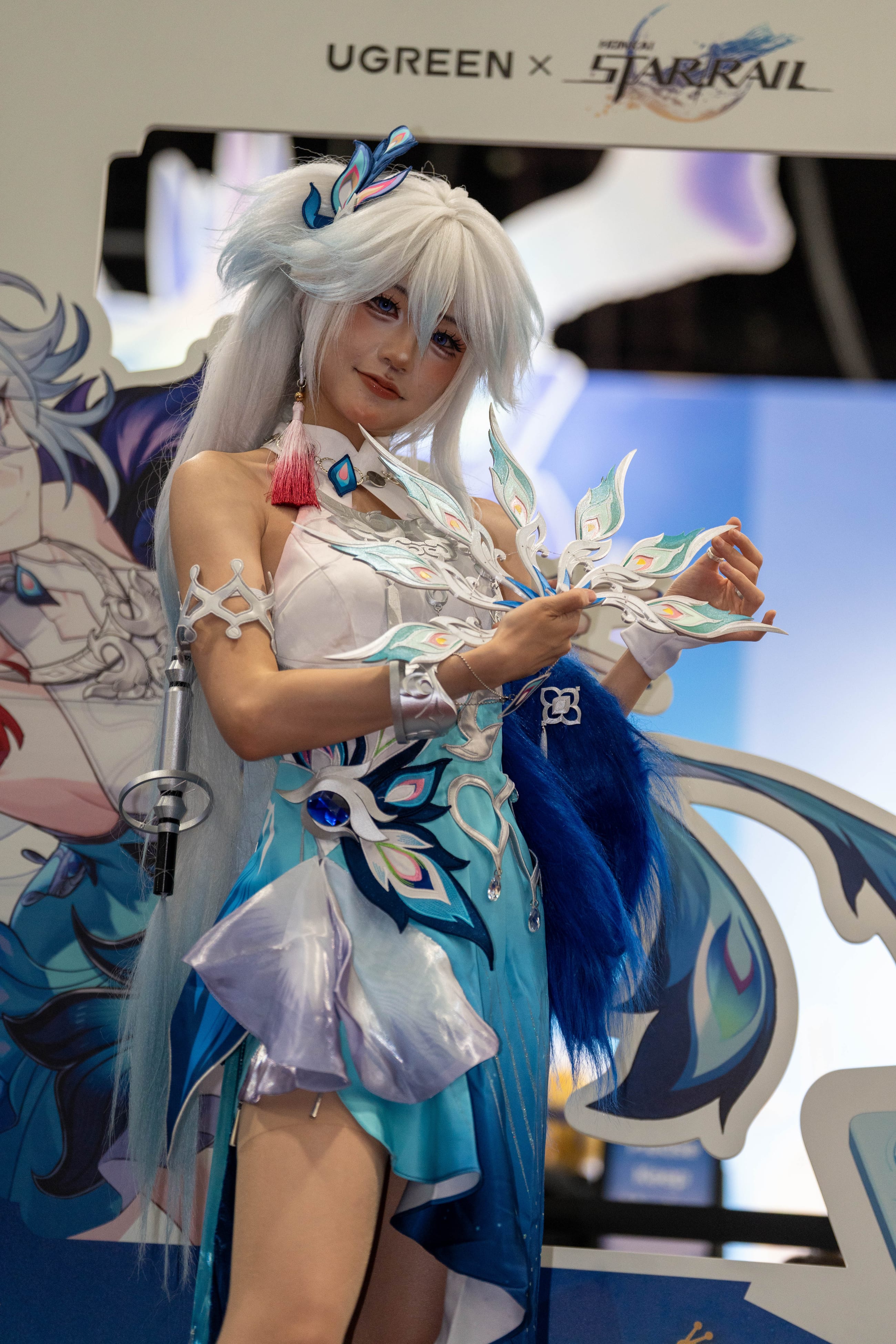 Cosplayer posing in front of a UGREEN x Honkai Star Rail activation wall, sponsor branding legible above her