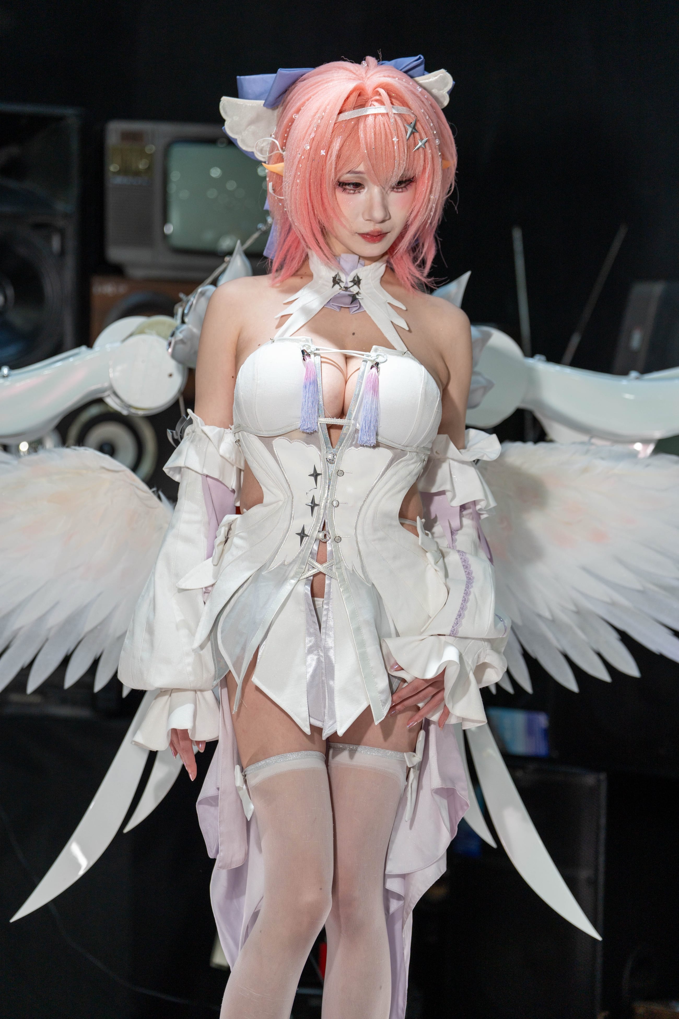 Cosplayer in a white winged costume standing before a wall of stacked vintage televisions