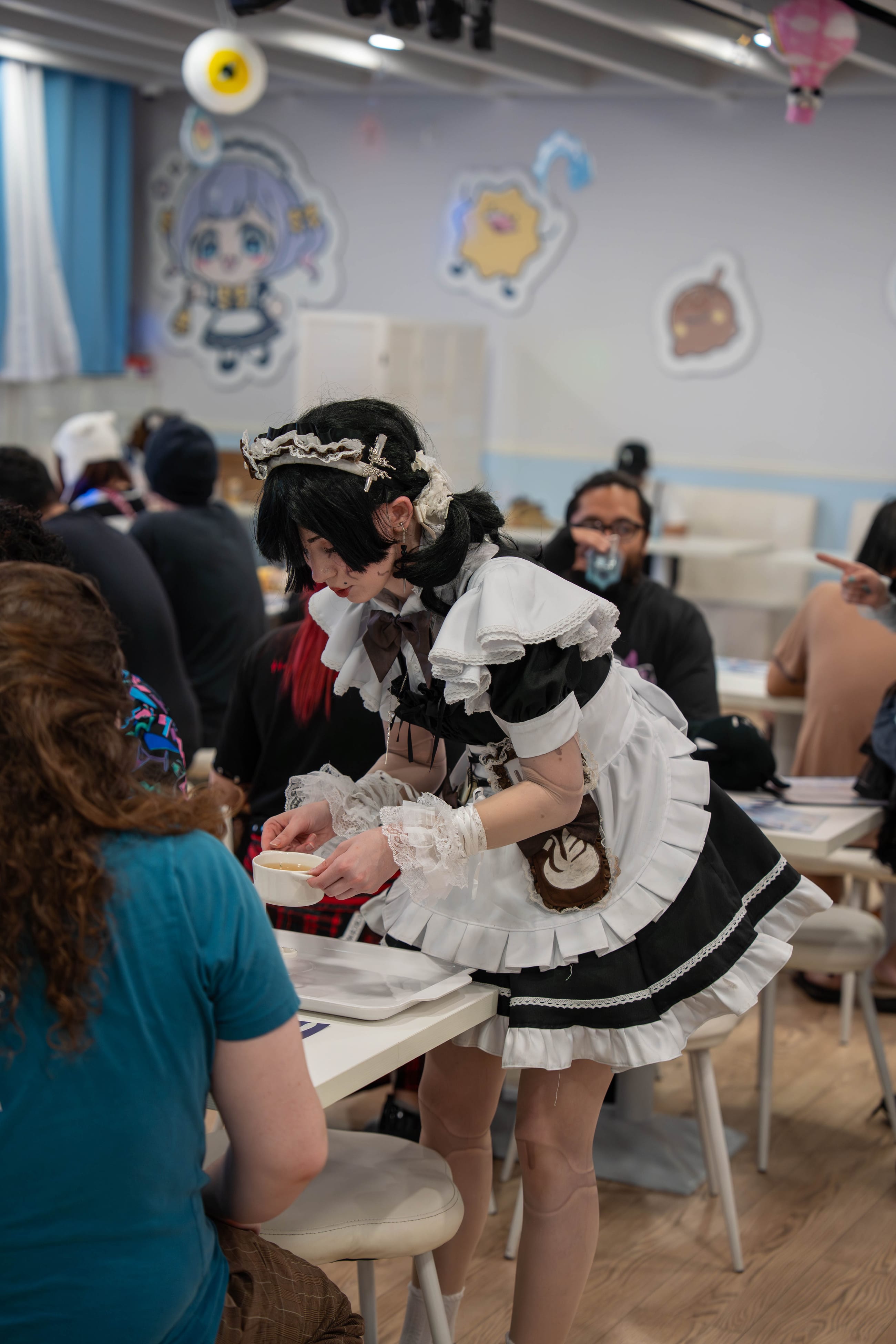 Maid cafe interior with staff in uniform working between pastel-painted walls and a service cart