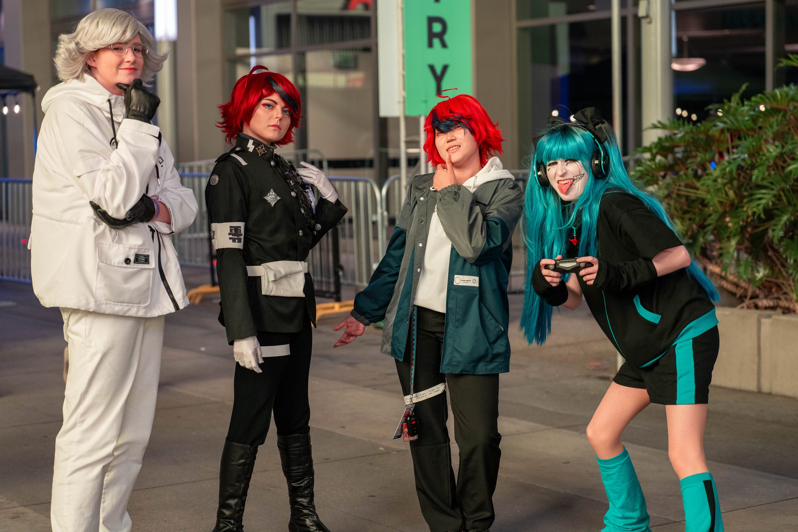 Four cosplayers outdoors in daylight beside the convention center, in teal, red and white uniforms