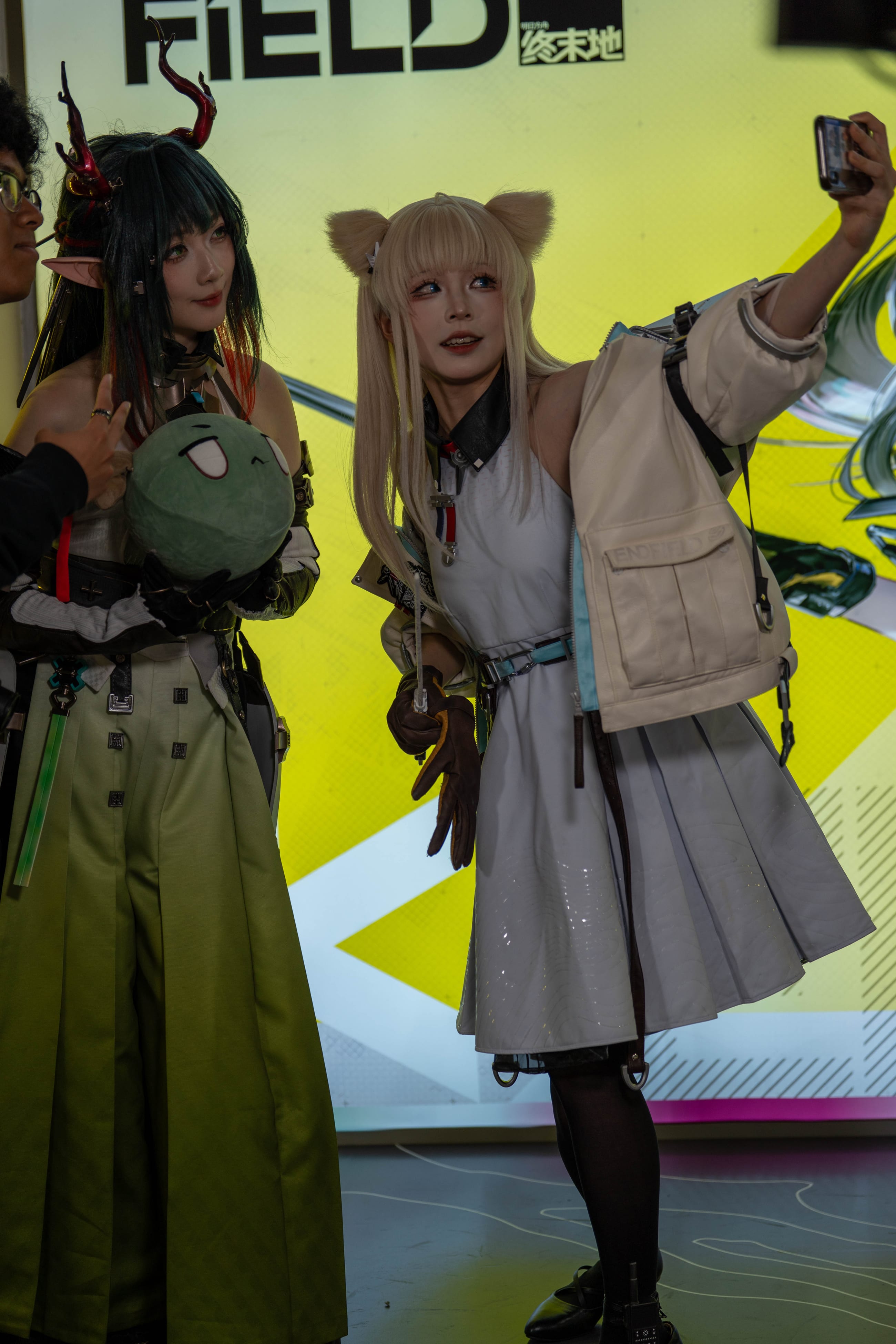 Two cosplayers taking a selfie in front of a bright yellow FIELD booth wall