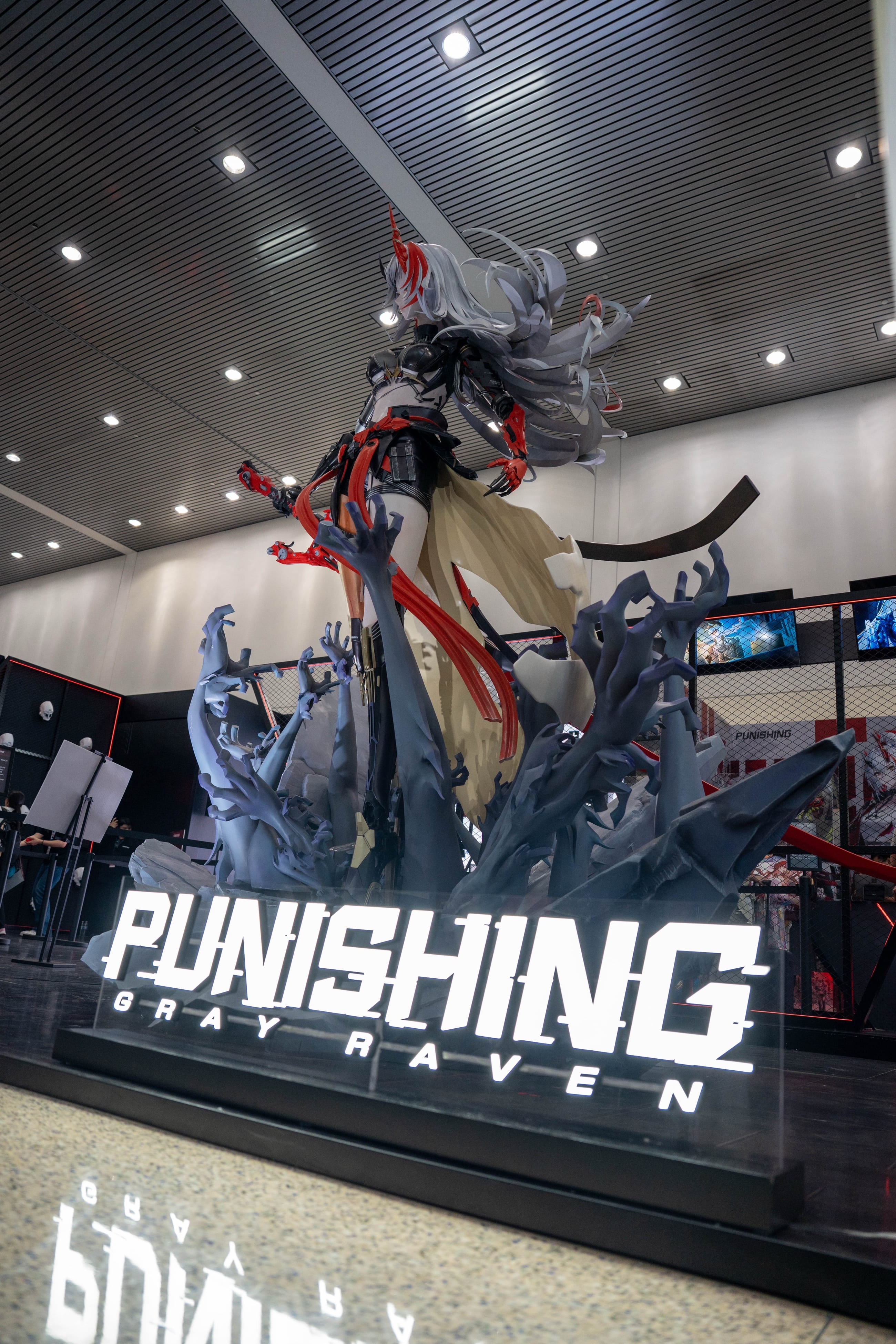 Full-height Punishing: Gray Raven statue lit from above, the game wordmark reading across the floor plinth beneath it