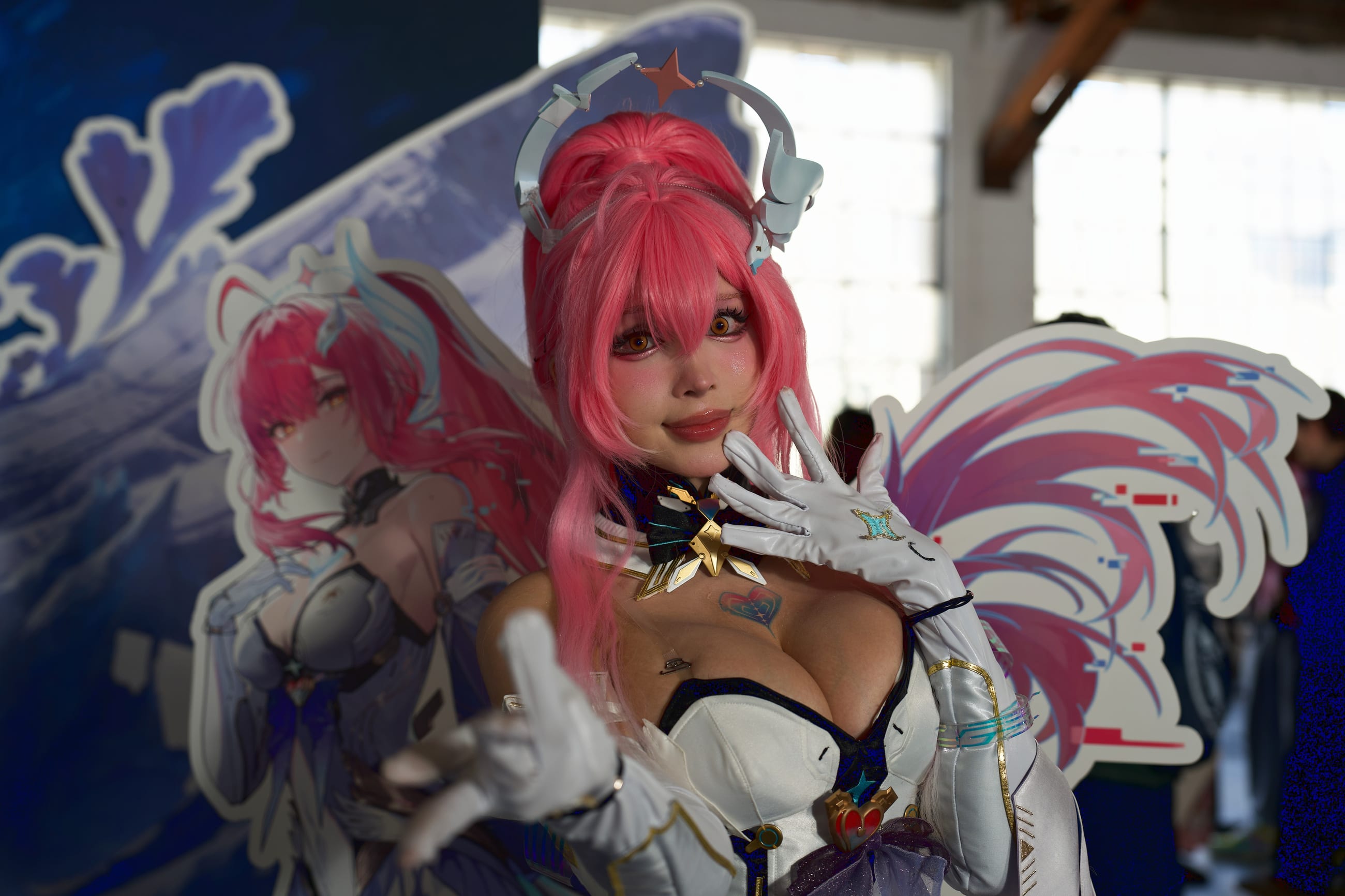 Cosplayer in a pink-winged stage costume, close, under the rig lighting the main stage