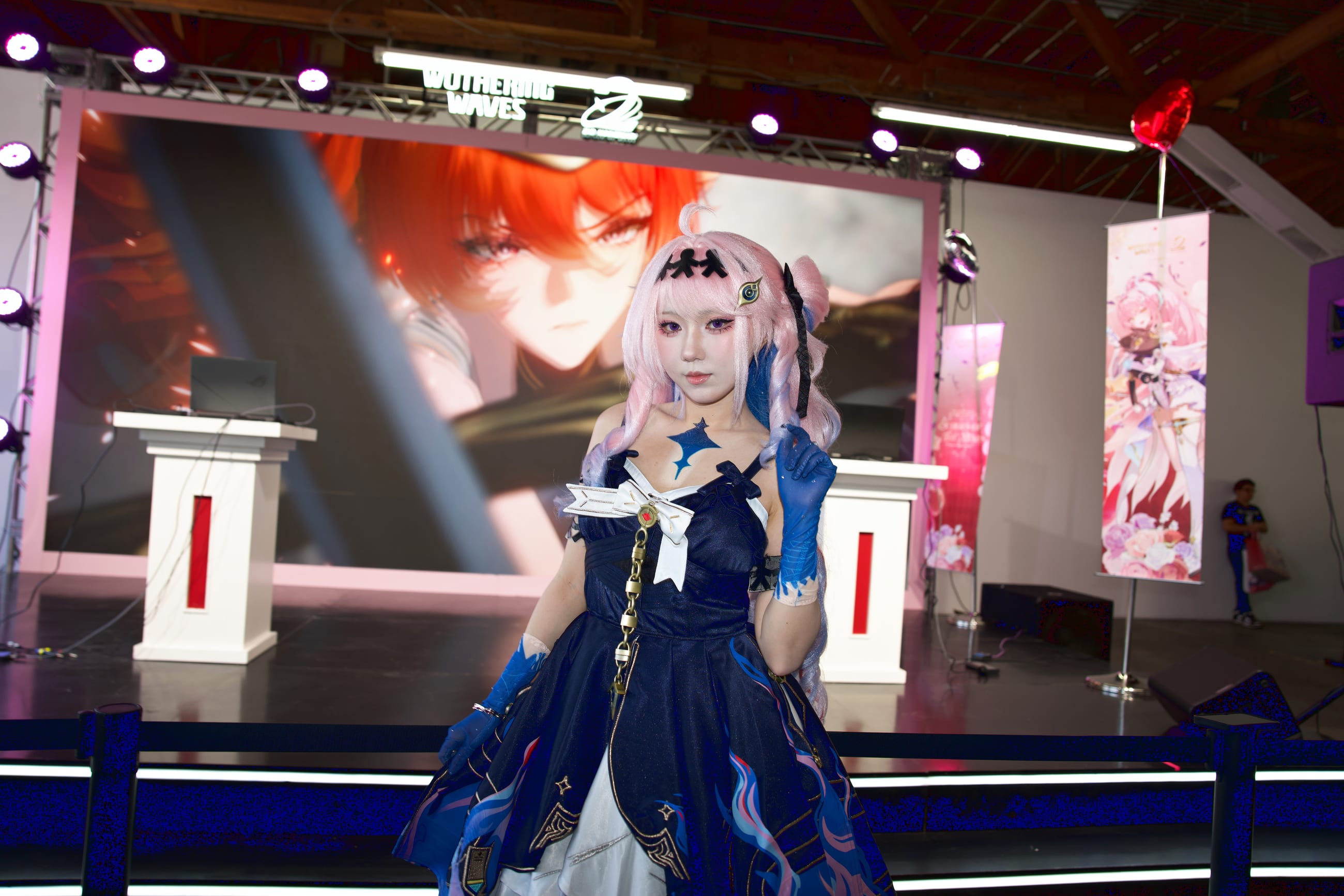 Cosplayer on the main stage between two podiums, key art filling the LED wall behind
