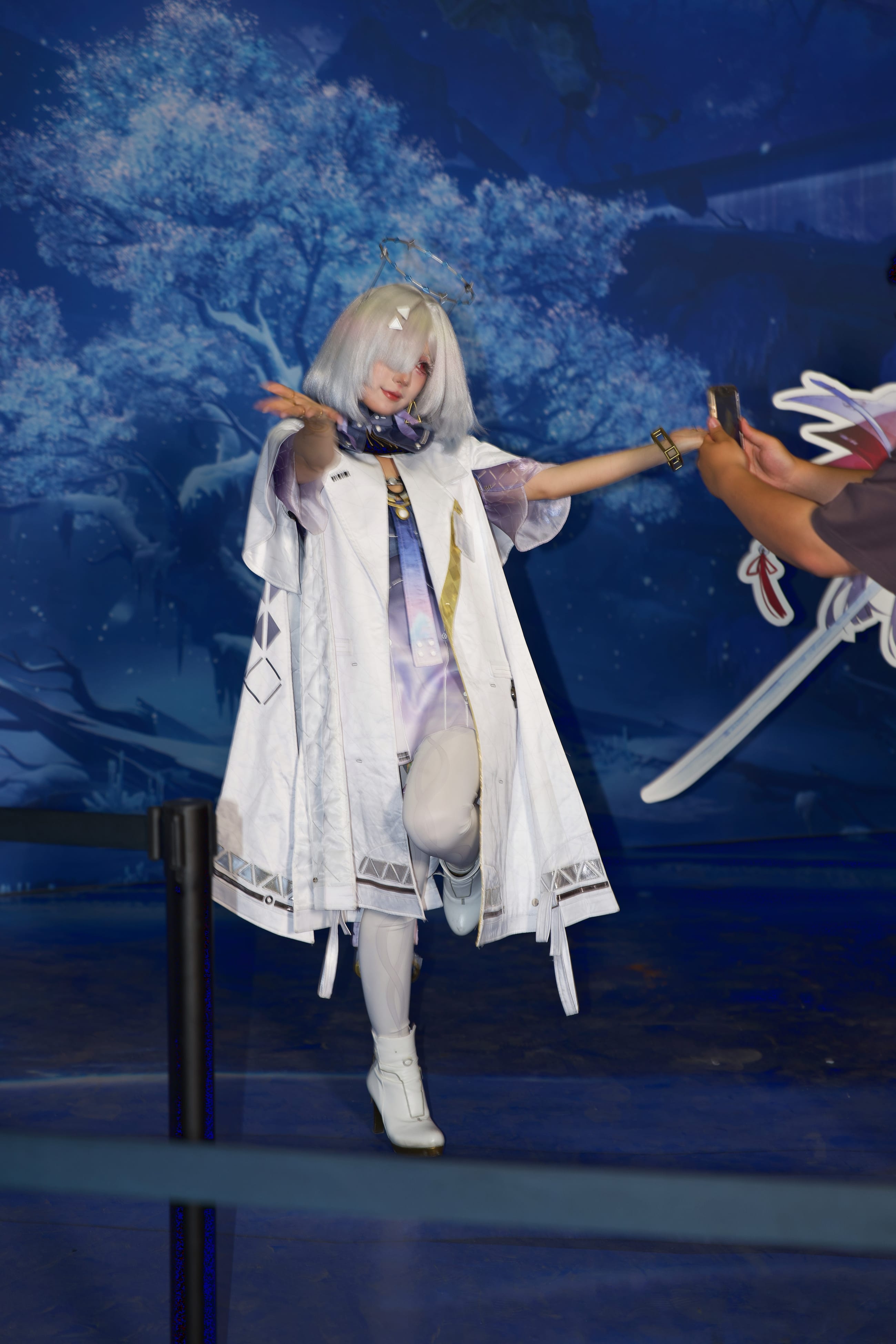 Cosplayer in a long white coat drawing a sword, arm extended, against the deep blue set