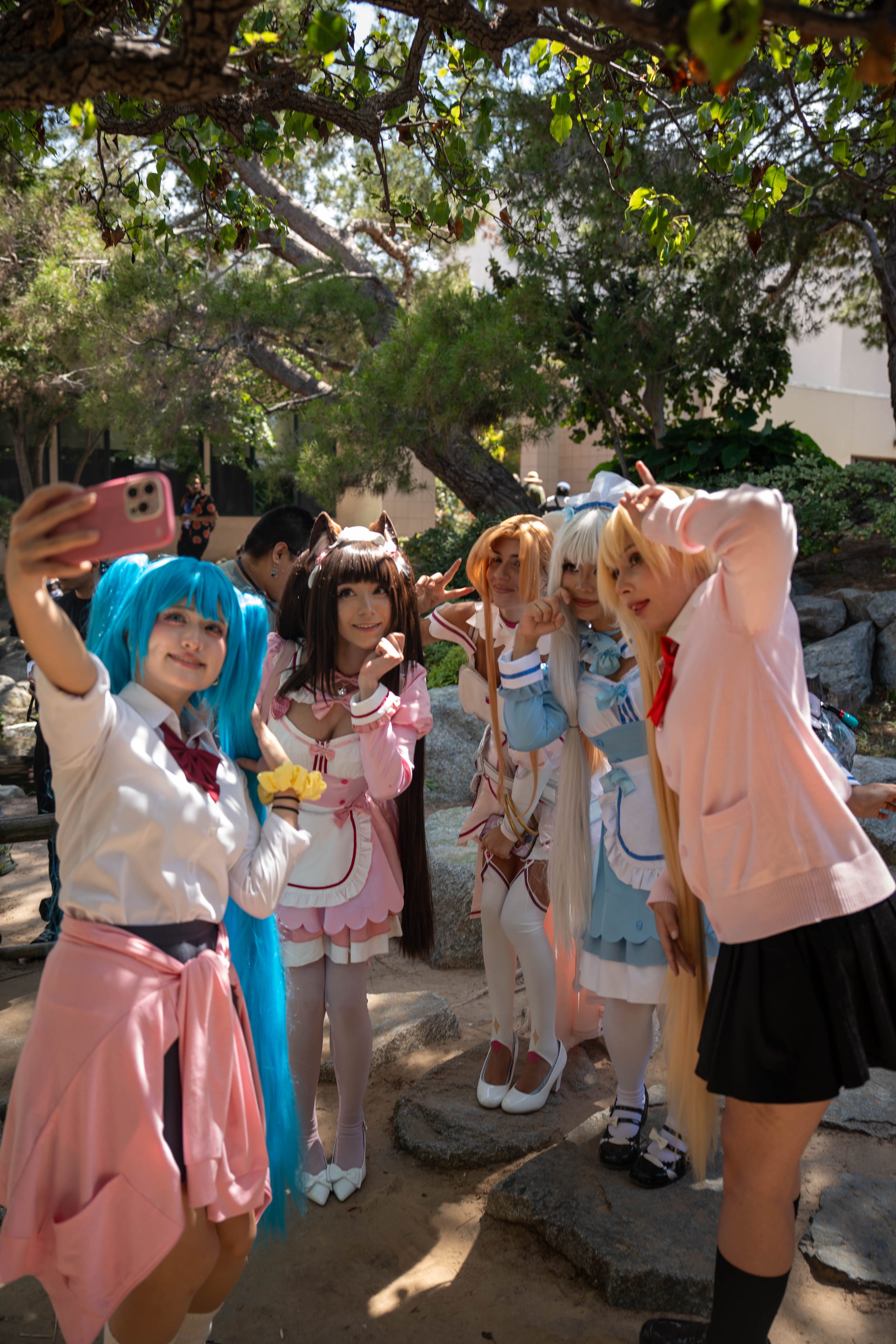 Cosplayers greeting each other with arms raised, dappled daylight through trees